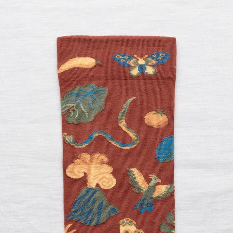 Close up of a sock in red and orange tones featuring a volcano pattern with animals.