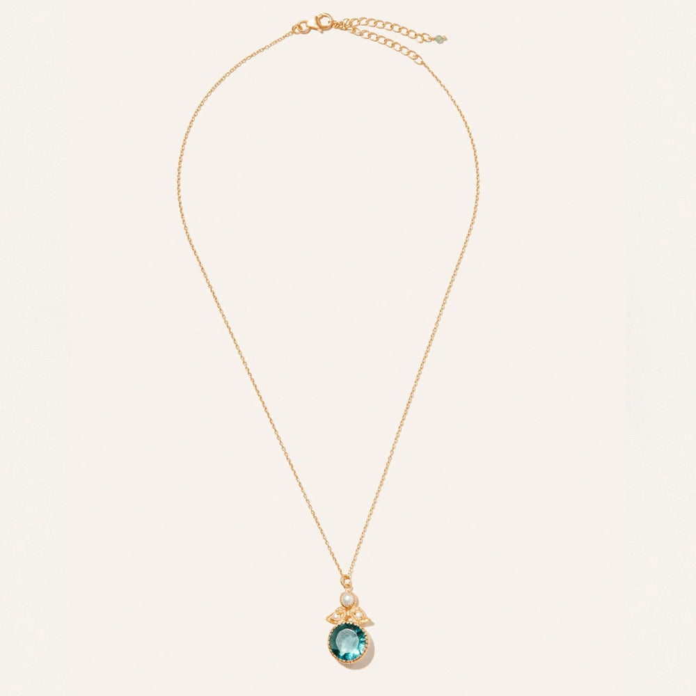 A delicate gold chain necklace with a small oval pendant featuring a light blue green stone and tiny clear accent stones, displayed on a clean off white background.