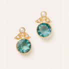 A pair of gold drop earrings featuring large round faceted teal-blue gemstones, small white pearl accents, and delicate gold leaf-like details, set against a clean off-white background.