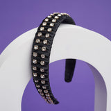A black headband with fabric ruffles and silver crystals balances on a white arch.