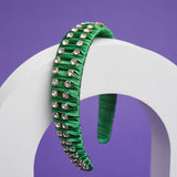 A green headband with fabric ruffles and silver crystals balances on a white arch.