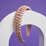 A pink headband with fabric ruffles and silver crystals balances on a white arch.