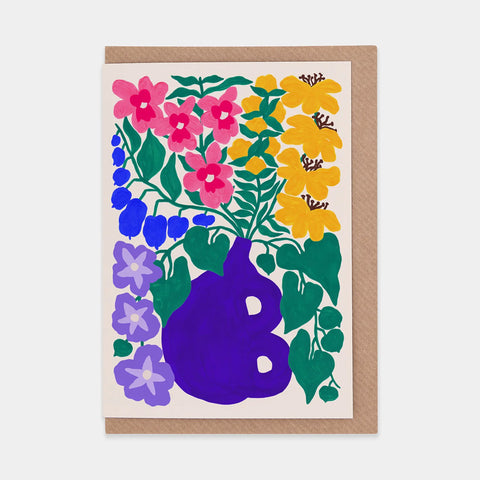 Multicoloured flowers and green leaves and stems coming out of an indigo "B" shaped vase on a white background.