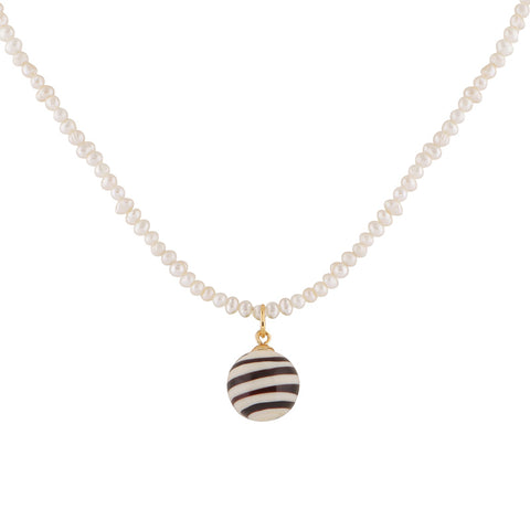 A black and ivory striped glass ball pendant hangs from a pearl strand necklace. 