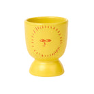Yellow ceramic egg cup with a sun face design on a white background