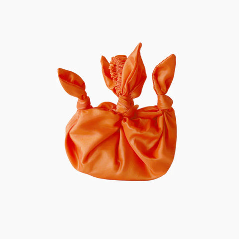 A round orange coloured satin bag with knot details and a scrunchie style handle.