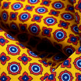 A close up of a yellow scarf showing small blue and red geometric designs. 