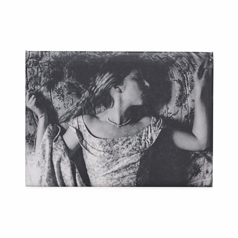 Rectangular magnet featuring a black and white photograph of a woman in a dress and pearl necklace lying down. 