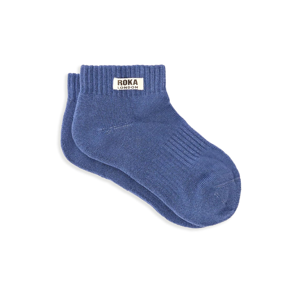 A pair of ribbed socks in blue with a white label and the words roka london against a white background
