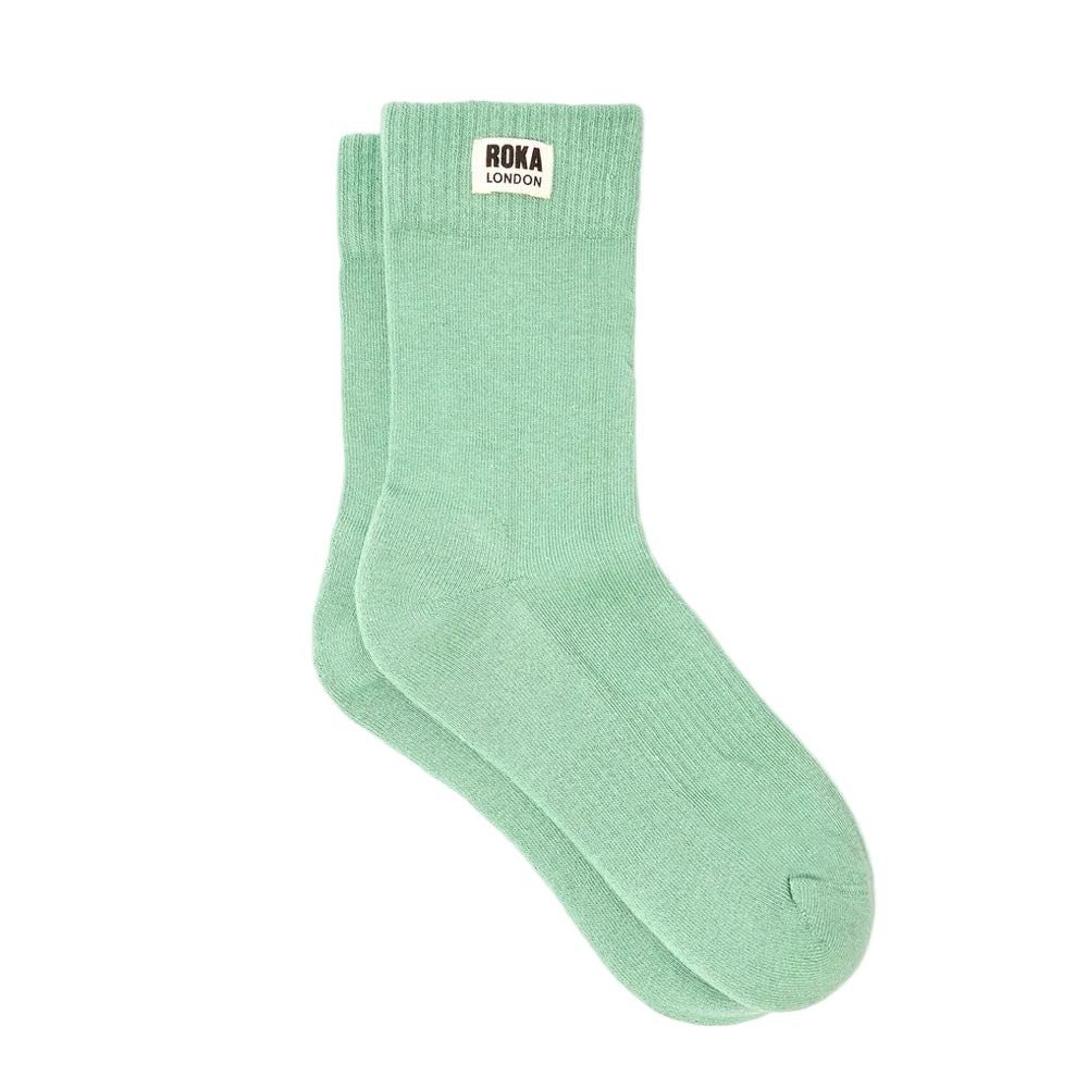A pair of mint green crew socks with a white 'roka london' label on the cuff, displayed against a clean white background.