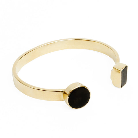 An open gold bangle with black shaped end detailing.  