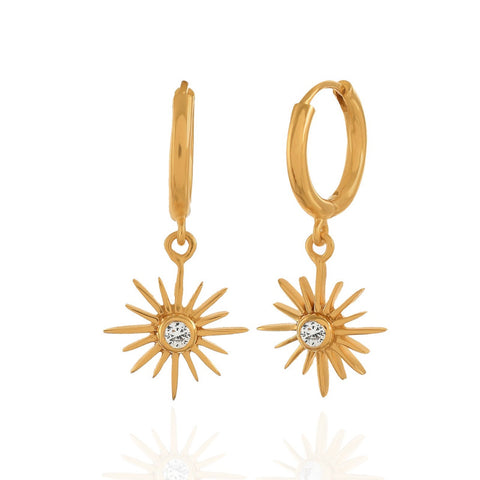 Felicity star crystal clear earrings hanging from a gold huggie band.