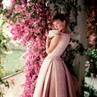 Photograph of Audrey Hepburn in pink dress in front of pink blossoms by Norman Parkinson, 1955.