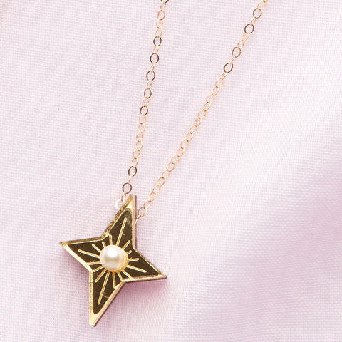 gold four-pointed star pendant with a pearl in its centre on a gold chain